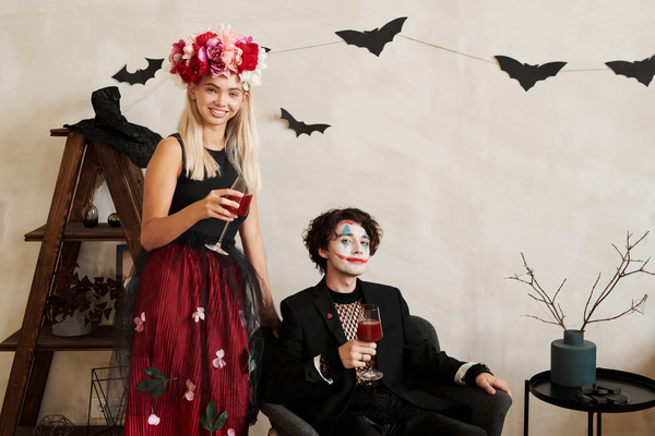 Woman with Wreath and Man with Joker Makeup on Background of Zone Decorated for Halloween